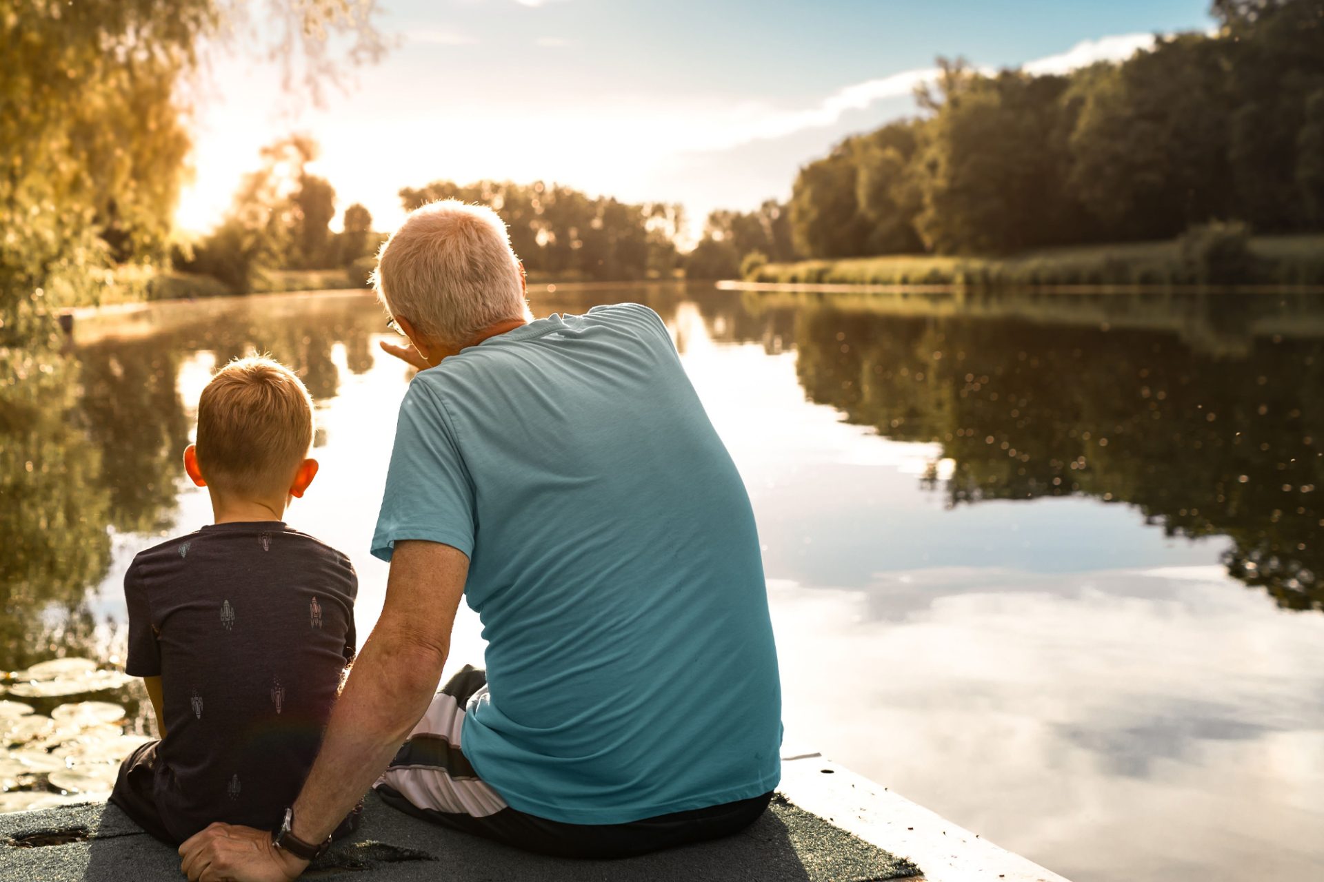 Grandfather and grandson sitting on dock looking at lake