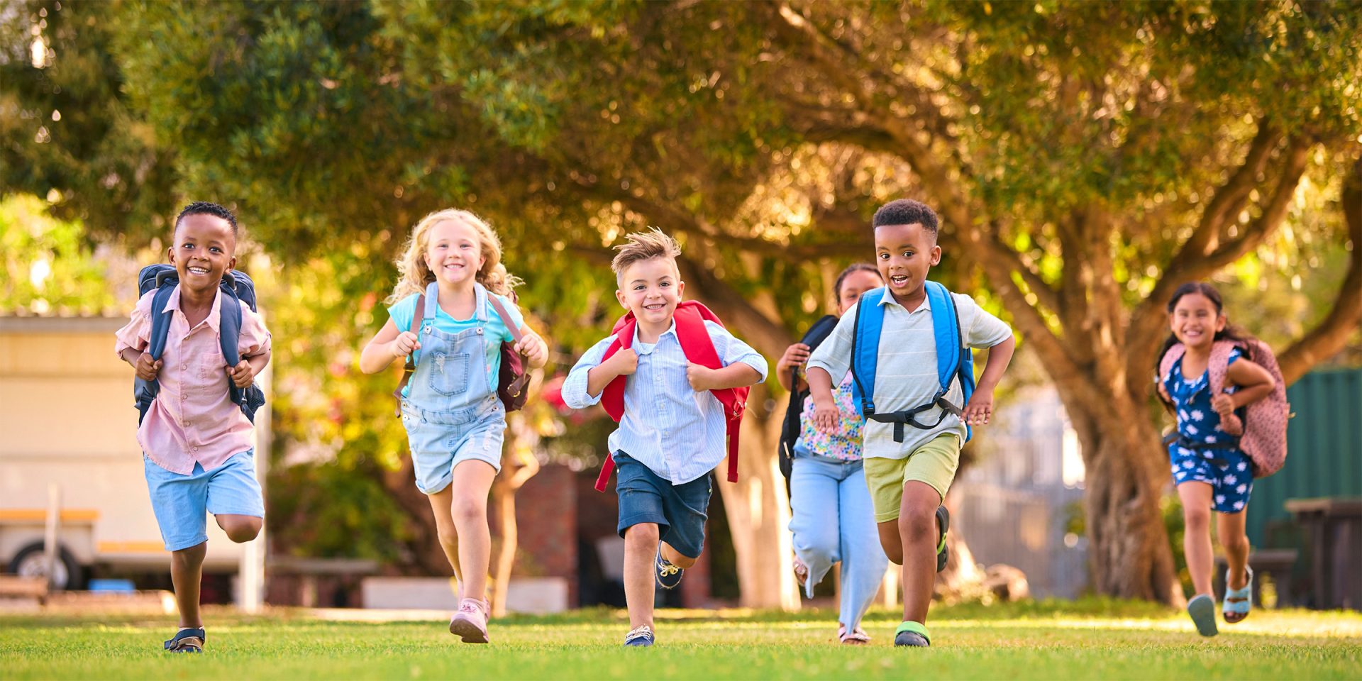 group of smiling children running outside with backpacks on