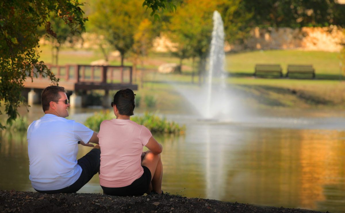 Happy couple sitting on the edge of the community pond